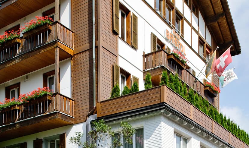 Hotel Bristol Adelboden building exterior with wooden balconies, red flowers, and Swiss flags.