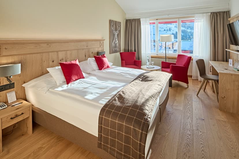 Hotel room with twin beds, wooden furniture, and snowy mountain view in Adelboden