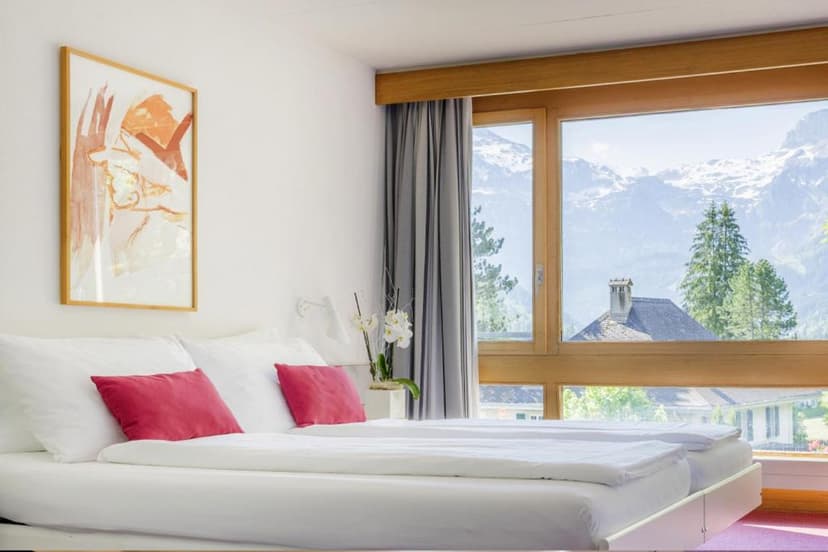 Hotel room with white bedding and view of snow-capped alpine mountains.