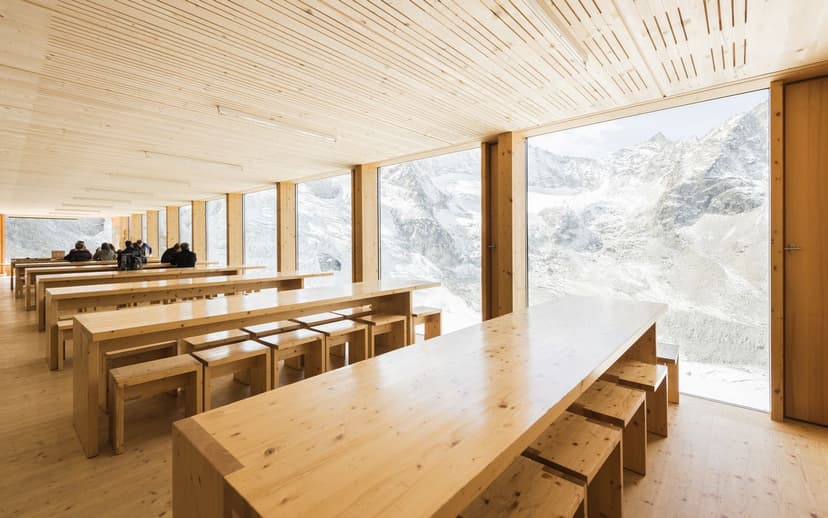 Wooden dining hall with long tables overlooking snowy alpine mountains at Cabane de Moiry CAS.