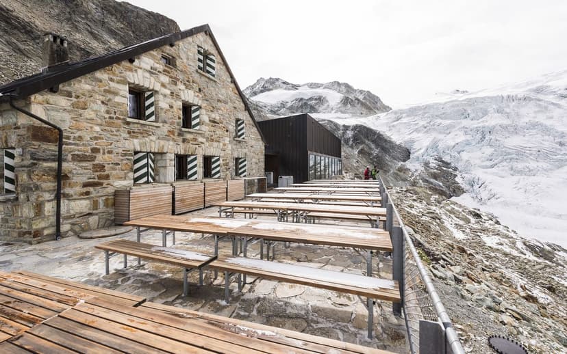Stone mountain hut with outdoor seating facing a large glacier at Cabane de Moiry CAS.