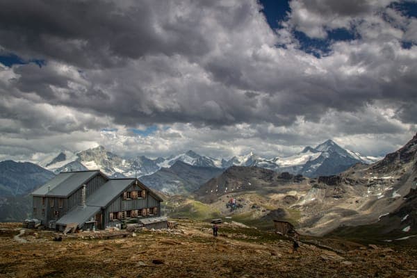 Mountain hut Cabane des Becs de Bosson beneath dramatic clouds and snowy peaks