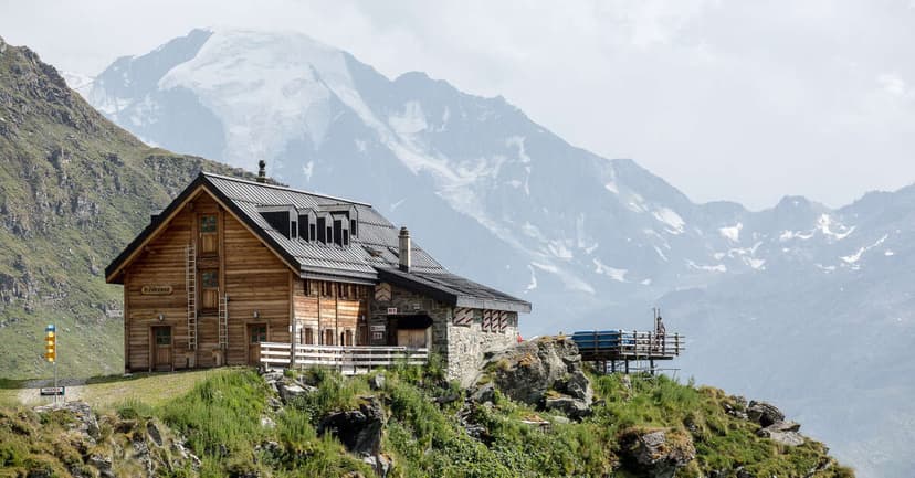 Wooden mountain refuge Cabane Mont Fort on grassy slope with snow-capped peaks in background