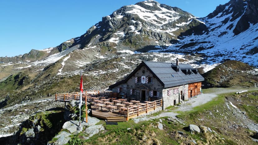 Stone mountain refuge with outdoor dining deck below snow-dusted peaks, Cabane Mont-Fort.