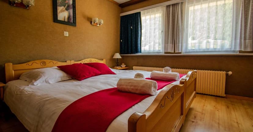 Bedroom with wooden bed, white linens, red accents, and windows with sheer curtains at Hôtel l'Escale.
