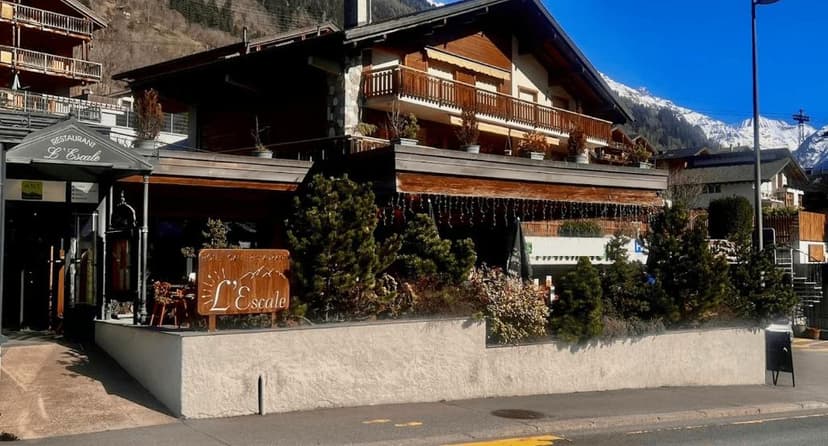 Restaurant L'Escale building with wooden balconies and snow-capped mountains in background.