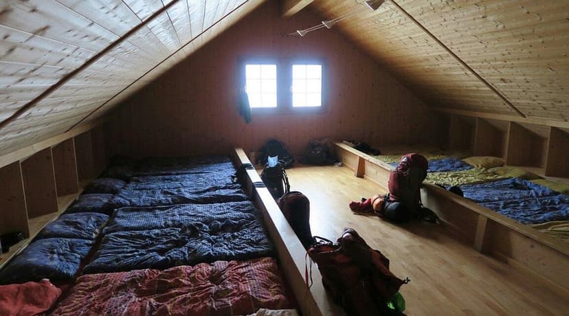 Sleeping loft in Cabane de Prafleuri with wooden walls, sleeping mats, and backpacks.