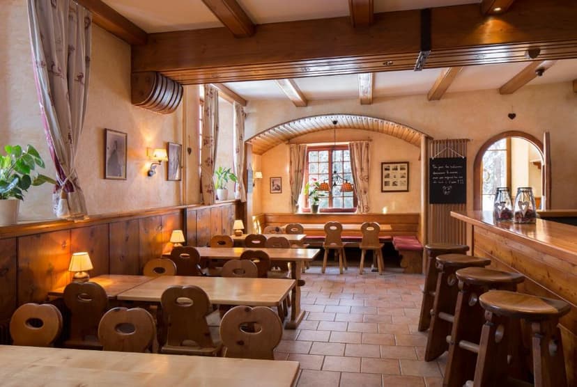 Rustic restaurant interior with wooden tables, chairs, bar stools, and exposed ceiling beams.