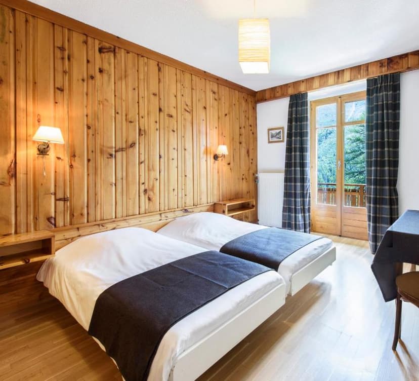 Twin beds in hotel room with wood paneling and balcony view of green mountains.