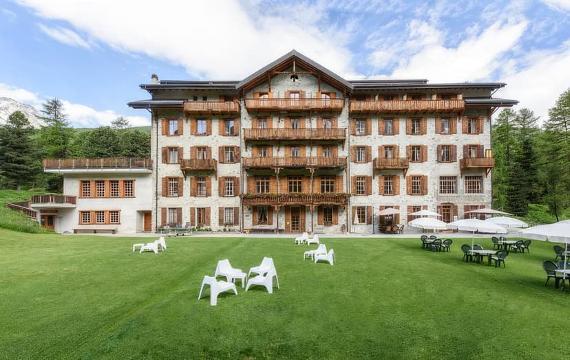 Grand Hotel & Kurhaus with wooden balconies and green lawn seating in a mountain setting.