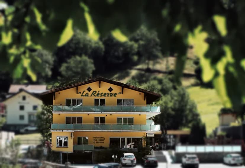 Yellow hotel building named "La Réserve" set against a lush green mountain backdrop.