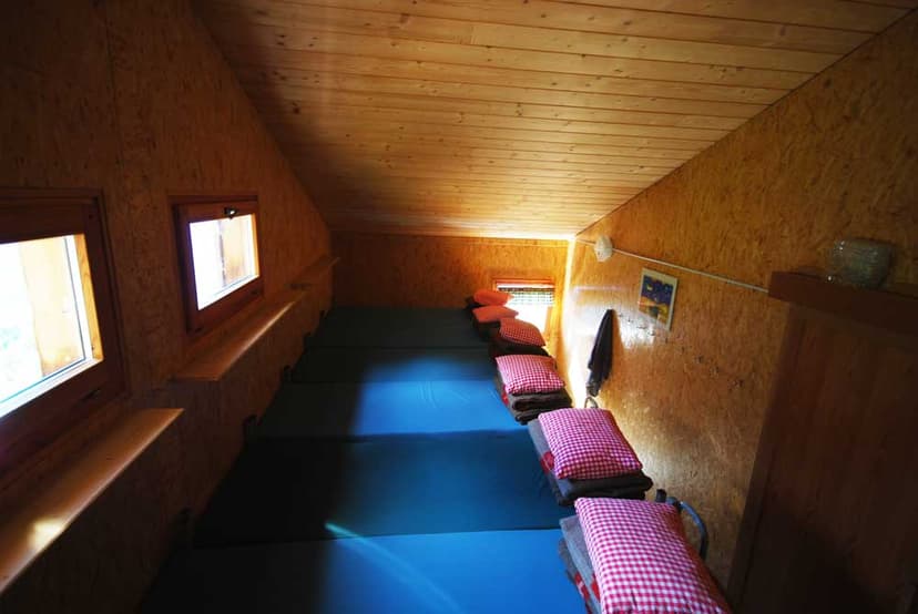 Sleeping loft with wooden walls, blue mats, and red gingham pillows in a mountain hut.