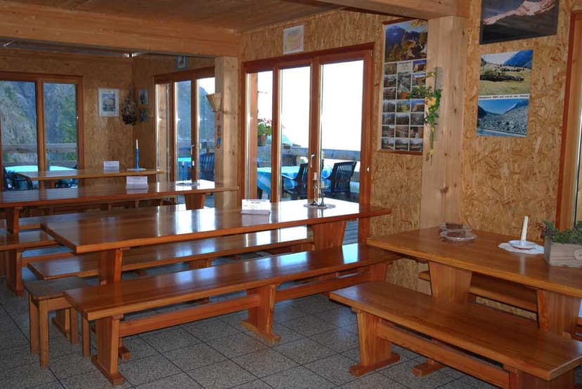 Interior dining area with wooden tables and benches, view of mountains through glass doors.