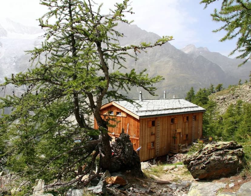 Wooden mountain hut nestled among trees with rugged peaks in the background