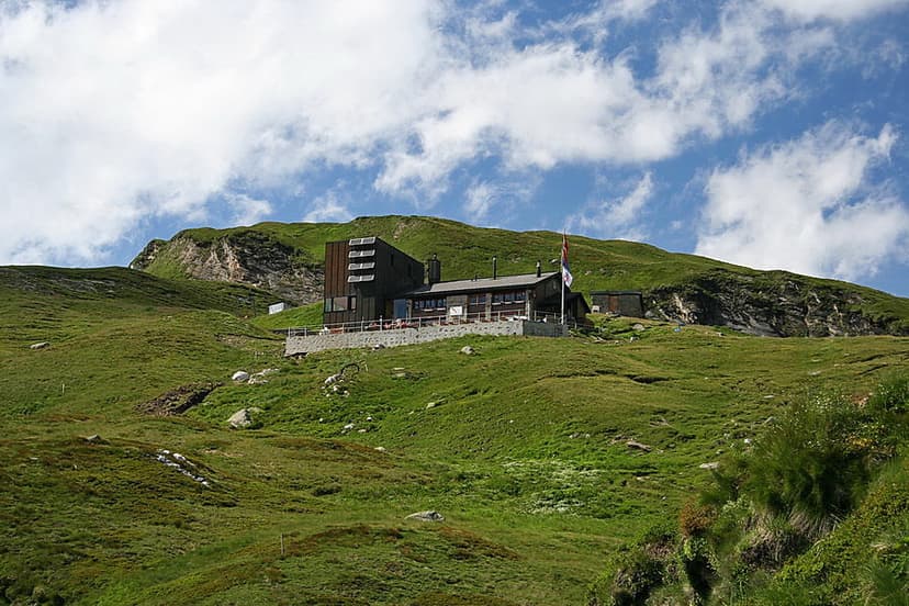 Mountain hut Capanna Michela Motterascio on grassy alpine slope under blue sky