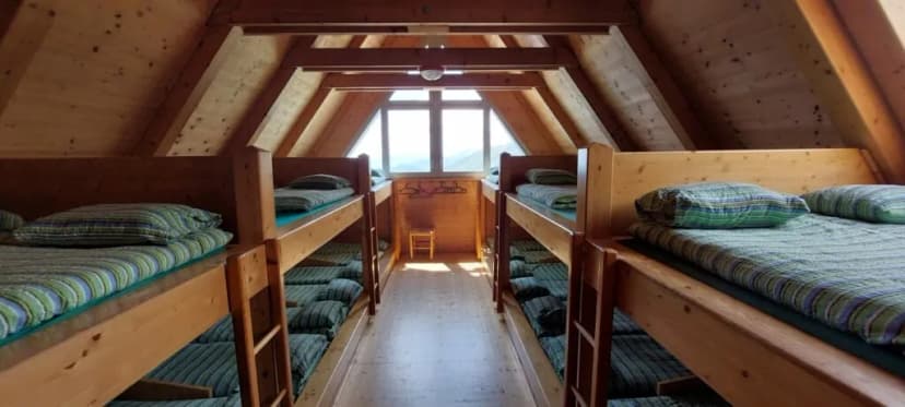 Bunk beds in a wooden alpine hut attic room with a window view of mountains