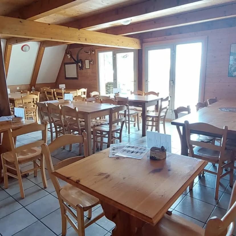 Rustic restaurant interior with wooden tables, chairs, and exposed beams, bright light from glass doors.
