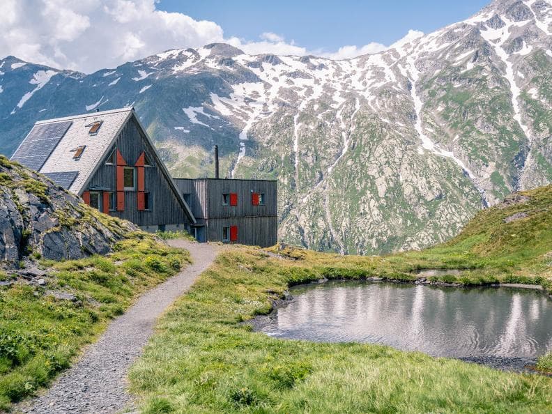 Mountain hut near small pond with snow-capped mountains in background