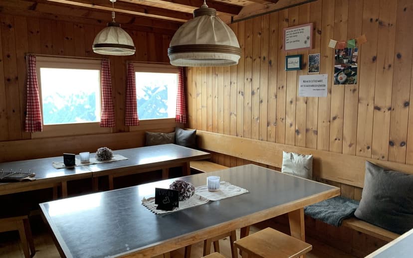 Interior of Ringelspitzhütte with wood paneling, metal tables, and mountain view through windows.