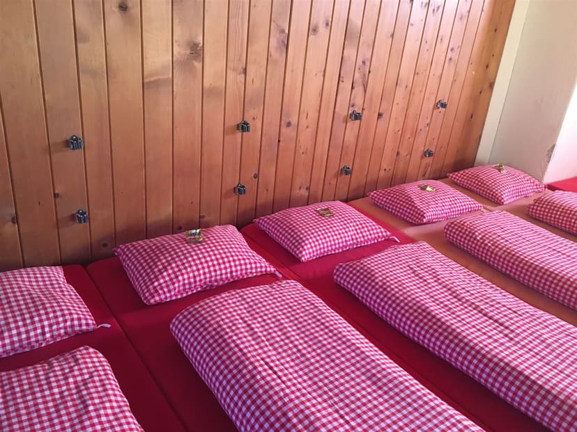 Bunk beds with red mattresses and red gingham bedding against a wood-paneled wall at Calandahütte.
