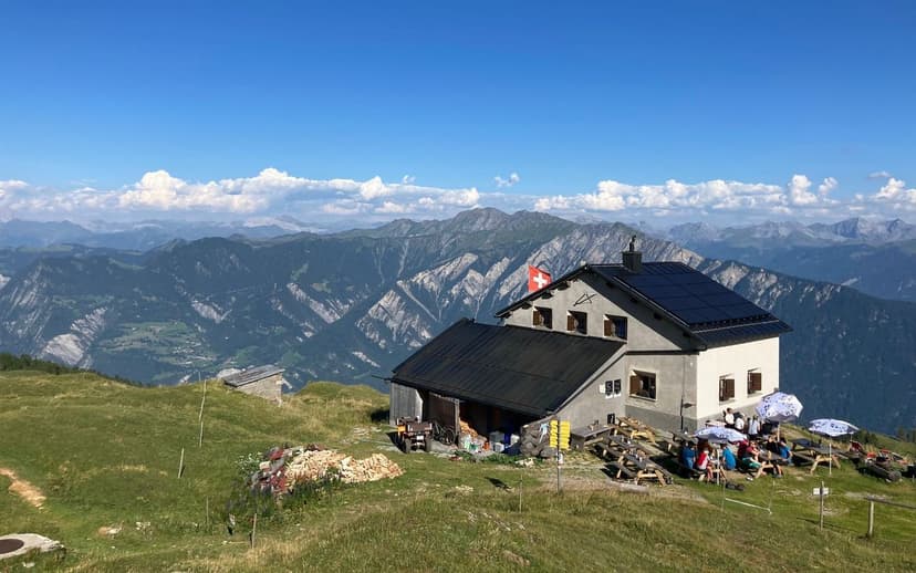 Calandahütte mountain hut with Swiss flag, hikers dining outdoors overlooking alpine peaks.