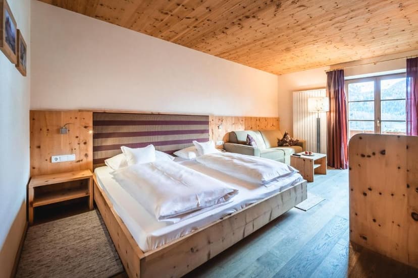 Hotel room with wooden ceiling, large bed, sofa, and mountain view through window