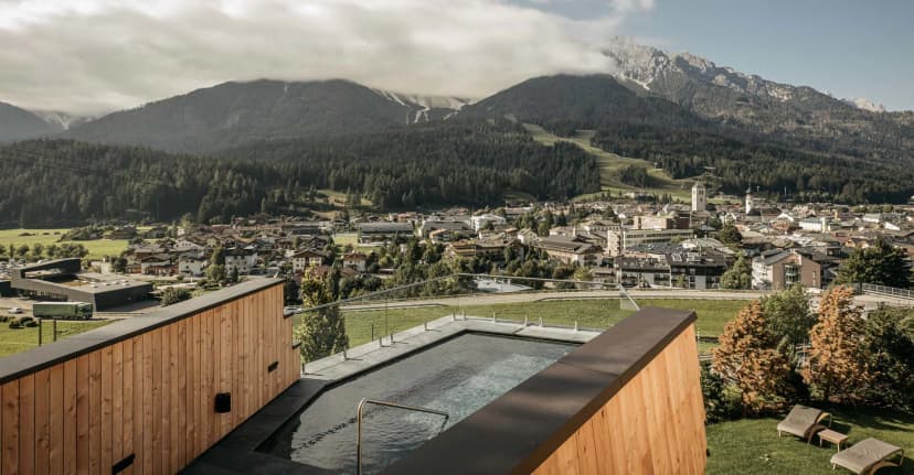 Outdoor pool overlooking alpine town and forested mountains, likely Naturhotel Leitlhof.
