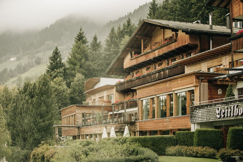 Wooden Naturhotel Leitlhof building with balconies against a foggy, forested mountain backdrop.
