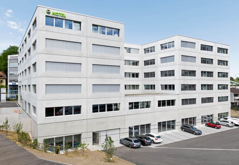 B&B Hotel St. Gallen building exterior with parking lot and cars under a clear blue sky.