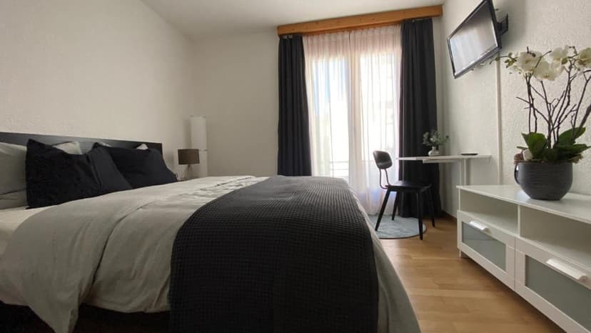 Bedroom with large bed, white furniture, wall-mounted TV, and orchid plant near window