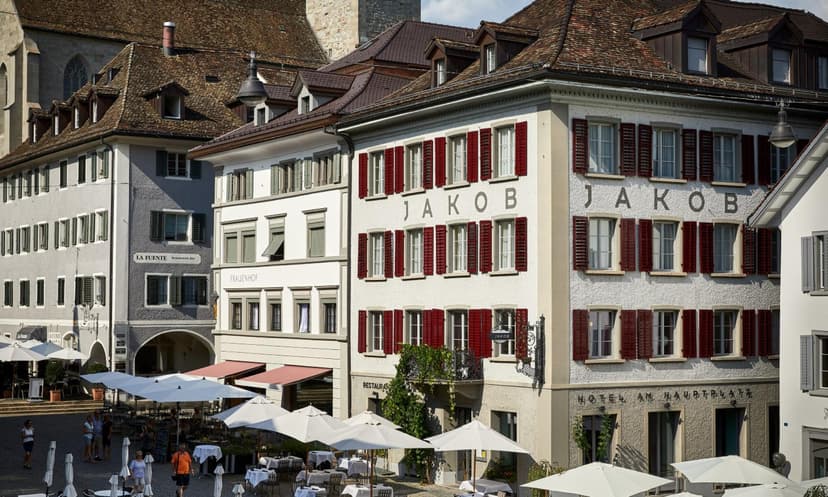 Hotel Jakob building with red shutters and outdoor cafe seating in a European town square.