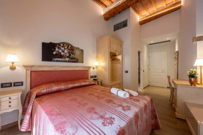 Bedroom with large bed, exposed wood ceiling beams, and floral artwork above the headboard.