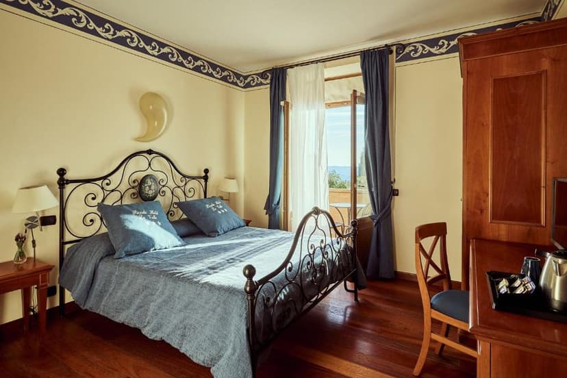 Bedroom with wrought iron bed, blue linens, and balcony view at Piccolo Hotel La Valle