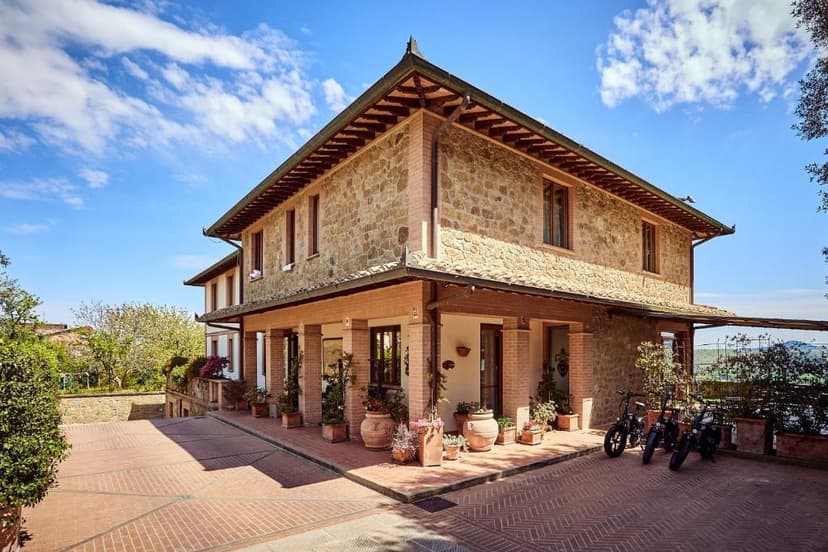 Stone hotel building with terracotta courtyard and three parked scooters under a blue sky.