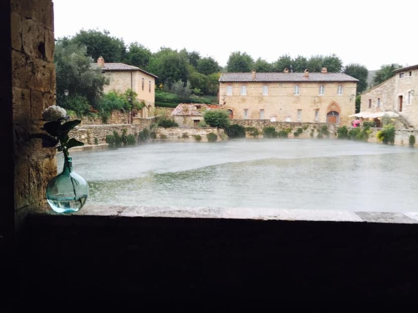 Hot spring pool steaming in Bagno Vignoni with a flower in a glass vase in the foreground.
