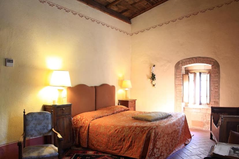Bedroom in Bagno Vignoni with orange bedspread, warm lighting, and arched window.