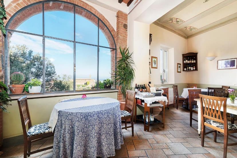 Dining room interior with large arched window overlooking greenery and a distant structure.