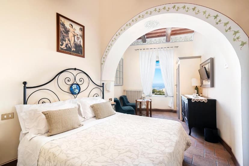 Bedroom in Albergo Il Giglio with wrought iron bed and view of distant landscape.