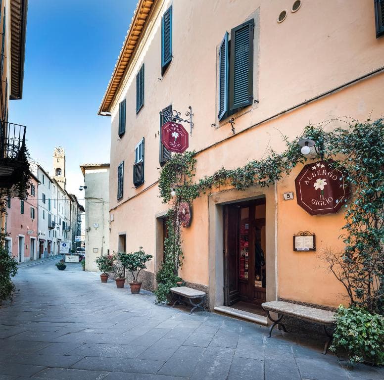 Albergo Il Giglio entrance on narrow stone street with historic buildings and tower in distance.