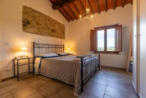Bedroom with wrought iron bed, stone accent wall, and window overlooking green fields in Albergo Roma.
