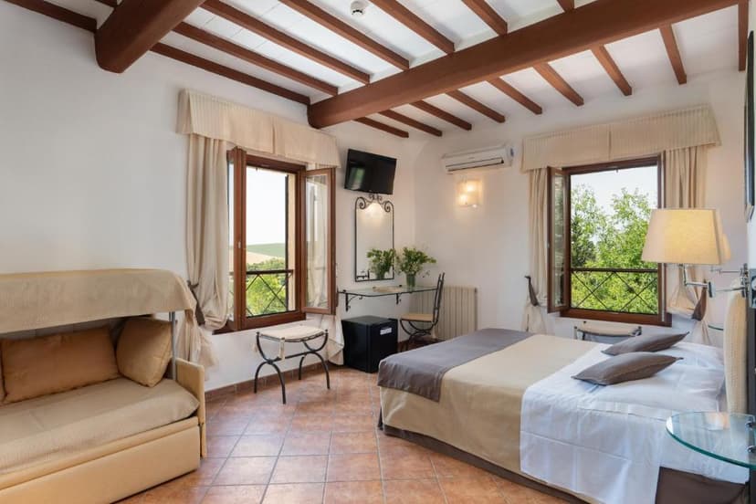 Hotel room with exposed wooden beams, terracotta floor, and view of green countryside.