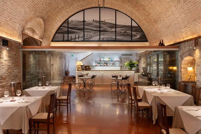 Dining room with brick arches, set tables, and a bar area featuring a Tuscan landscape mural.