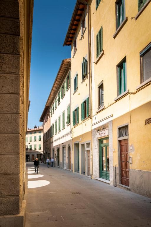 Narrow stone street lined with yellow buildings with green shutters under a clear blue sky.