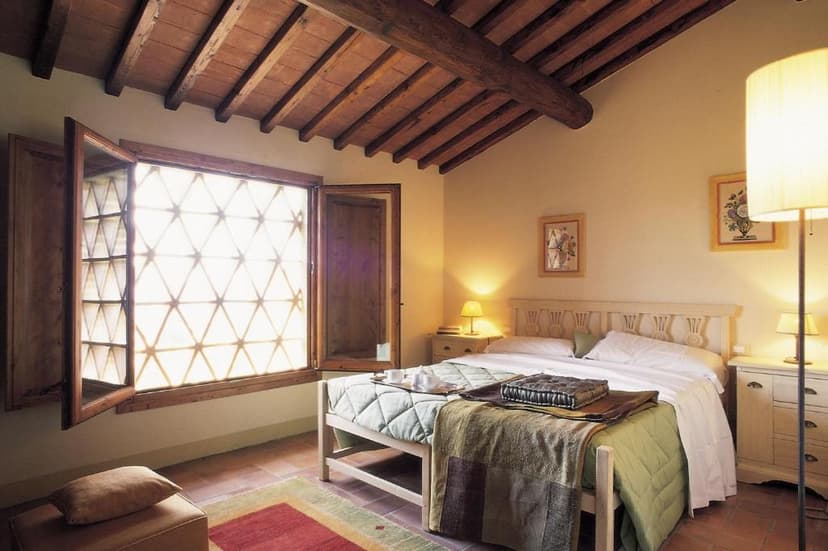 Bedroom with exposed wooden beams, white bedding, and a window casting triangular light patterns.