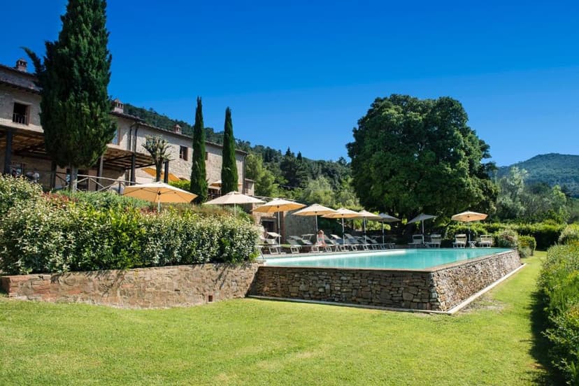 Swimming pool with stone wall, lounge chairs, and umbrellas near a stone building in Gambassi Terme.
