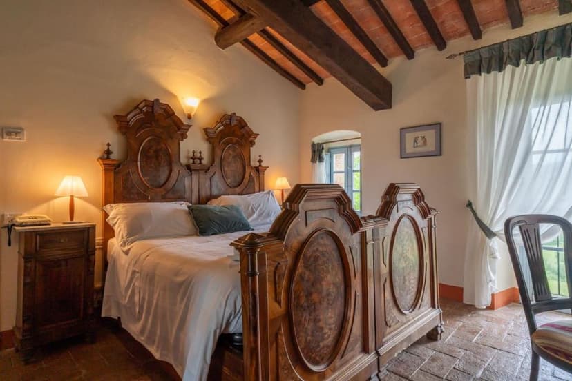 Bedroom with large antique wooden bed, exposed wooden beams, and terracotta floor tiles in Monteriggioni.