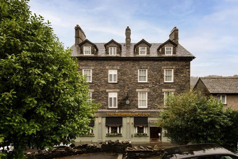 Stone building exterior of The Temperance Inn with lush green trees and blue sky.
