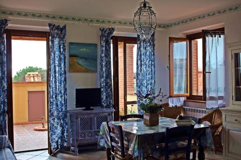 Dining area with blue floral curtains, wicker chairs, and view of a tiled terrace.