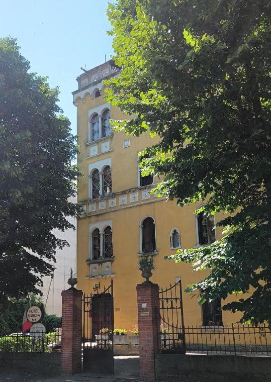 Yellow historic building facade partially hidden by lush green trees, Hotel Europa sign visible.