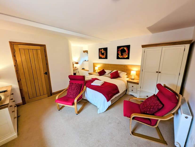 Bedroom with double bed, red accent chairs, white wardrobe, and wooden door.